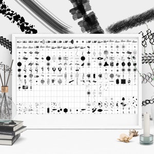 May include: A white framed poster with a grid of black and white brushstrokes and patterns. The poster is on a white surface with a vase of branches, a candle, and a stack of books.