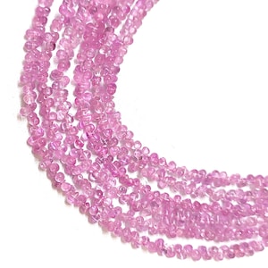 May include: Multiple strands of small, light pink, faceted gemstones. The beads are strung together, forming flowing lines against a white backdrop. The gemstones are uniform in shape and size, with a slightly translucent appearance.