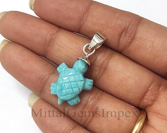 Könnte beinhalten: Ein türkisblauer Schildkrötenanhänger aus Edelstein mit einer silbernen Öse. Der Anhänger wird in einer Hand gehalten.