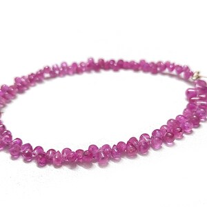May include: A strand of pink gemstone beads, likely ruby, strung on a thin wire. The beads are small and teardrop-shaped, creating a delicate and elegant look.