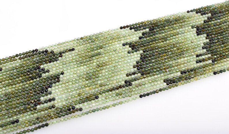 May include: A strand of green gemstone beads, each bead is round and faceted. The beads are strung on a clear thread and are ready for jewelry making.