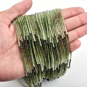 May include: A strand of green and black gemstone beads. The beads are small and round, and they are strung on a thin wire. The beads are arranged in a random pattern, and they are all about the same size.