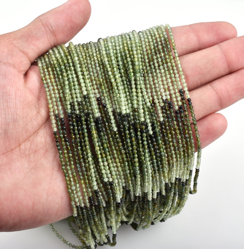 May include: A strand of green and black gemstone beads. The beads are small and round, and they are strung on a thin wire. The beads are arranged in a random pattern, and they are all about the same size.