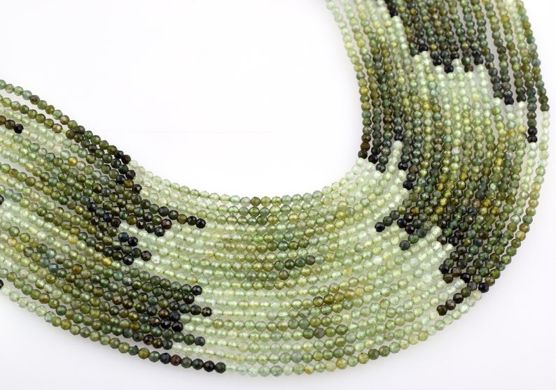May include: A strand of green and black faceted gemstone beads. The beads are round and have a smooth, polished finish.