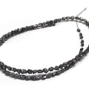 May include: A strand of black diamond beads, each bead is a rough, uncut diamond. The beads are strung on a thin wire and are ready to be used in jewelry making.