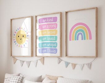 May include: A light pink, blue, and yellow rainbow with a white background. The rainbow is on a framed poster with a light wood frame. The poster is hanging on a white wall with a garland of flags above it. There are three posters in total, with the other two posters featuring a sun and a list of positive affirmations.