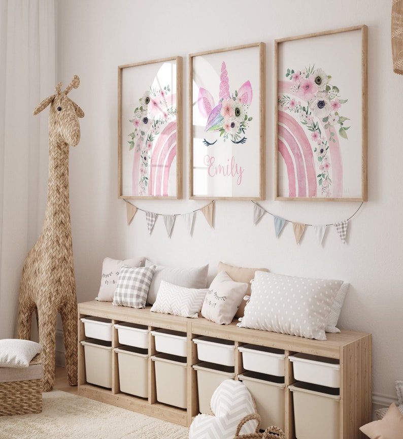 May include: Three framed watercolour prints featuring a pink rainbow with floral accents. The centre print has a unicorn face with a floral crown and the name "Emily" written below.