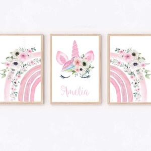 May include: Three watercolour prints featuring a pink rainbow with white flowers, a unicorn face with a floral crown, and the name Amelia.