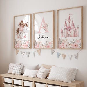 May include: Three framed art prints with a fairytale theme. One features a unicorn and a girl, another a pink letter "A" with "Autumn" below, and the last a pink castle. Floral accents and a banner complete the decor.