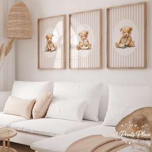 May include: Three framed art prints featuring watercolor illustrations of teddy bears. Each print has a light brown wooden frame and a background with vertical stripes. The teddy bears are depicted in various poses, with soft brown fur and seated on a white oval.