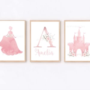 Pu&ograve; includere: Tre stampe ad acquerello rosa per una cameretta o una nursery. Le stampe presentano una silhouette di principessa, la lettera A con accenti floreali e un castello rosa con accenti floreali. Il nome Amelia &egrave; scritto sotto la lettera A.