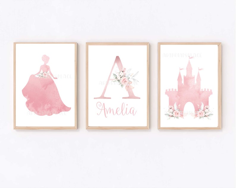 Pu&ograve; includere: Tre stampe ad acquerello rosa per una cameretta o una nursery. Le stampe presentano una silhouette di principessa, la lettera A con accenti floreali e un castello rosa con accenti floreali. Il nome Amelia &egrave; scritto sotto la lettera A.