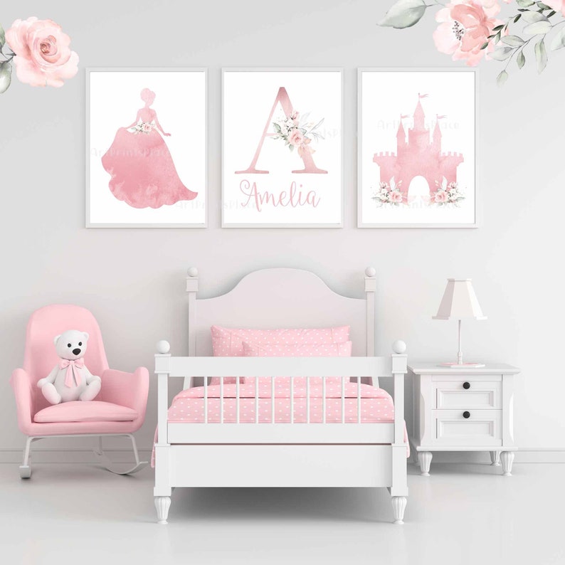 Pu&ograve; includere: Tre stampe ad acquerello rosa con una silhouette di principessa, la lettera A con accenti floreali e una silhouette di castello. La stampa della lettera A ha il nome Amelia scritto sotto.