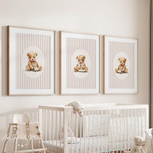 May include: Three framed prints featuring watercolor teddy bear illustrations. Each print has a beige and white striped background with an oval frame. The teddy bears are depicted in various poses, holding toys and wearing bows.