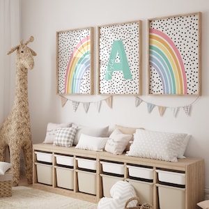 May include: Three framed prints featuring a rainbow and polka dot design. The centre print displays the letter A with the name Ayla written below. The prints are hung on a white wall above a wooden storage bench with white storage bins.