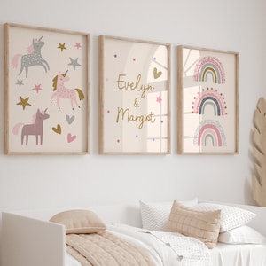 K&ouml;nnte beinhalten: Drei gerahmte Kunstdrucke mit hellbeigem Hintergrund. Einer zeigt Einh&ouml;rner, Sterne und Herzen. Ein anderer zeigt die Namen "Evelyn & Margot". Der dritte zeigt drei bunte Regenbogen.