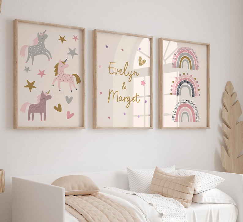 K&ouml;nnte beinhalten: Drei gerahmte Kunstdrucke mit hellbeigem Hintergrund. Einer zeigt Einh&ouml;rner, Sterne und Herzen. Ein anderer zeigt die Namen "Evelyn & Margot". Der dritte zeigt drei bunte Regenbogen.