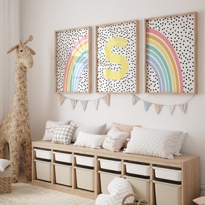May include: Three framed prints featuring a rainbow and polka dot design. The prints are hung on a white wall above a wooden bench with storage compartments. The bench is decorated with cushions and a stuffed giraffe.