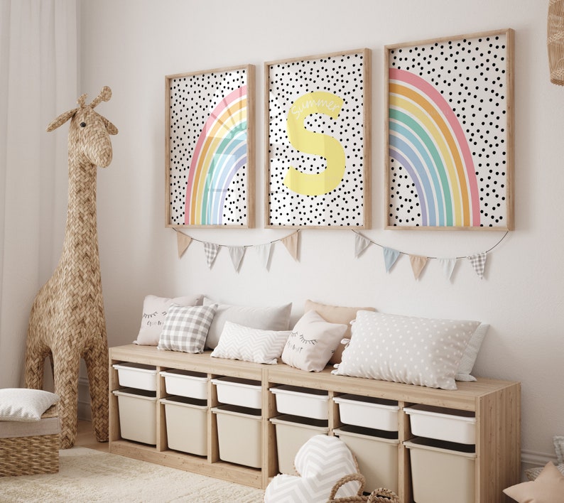 May include: Three framed prints featuring a rainbow and polka dot design. The prints are hung on a white wall above a wooden bench with storage compartments. The bench is decorated with cushions and a stuffed giraffe.