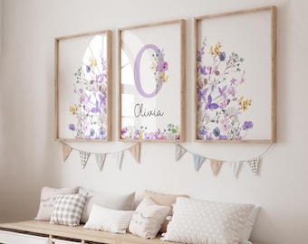 May include: Three framed prints featuring watercolour floral designs and the letter "O" in purple with the name "Olivia" underneath. The prints are hung on a white wall with a garland of flags below.