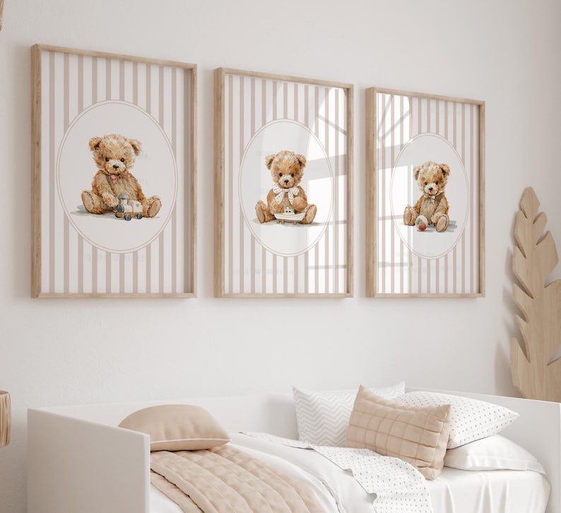 May include: Three framed prints featuring watercolor illustrations of teddy bears. Each bear is depicted in a different pose, set against a striped background within an oval frame. The frames are a light wood color, and the overall theme is suitable for a nursery or children's room.