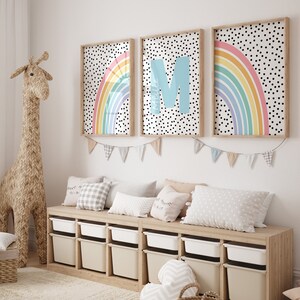 May include: A light wood storage bench with white bins and a white, grey, and black patterned cushion. Three framed prints with rainbow designs and black polka dots hang above the bench. The prints feature the letters "M" and "A".