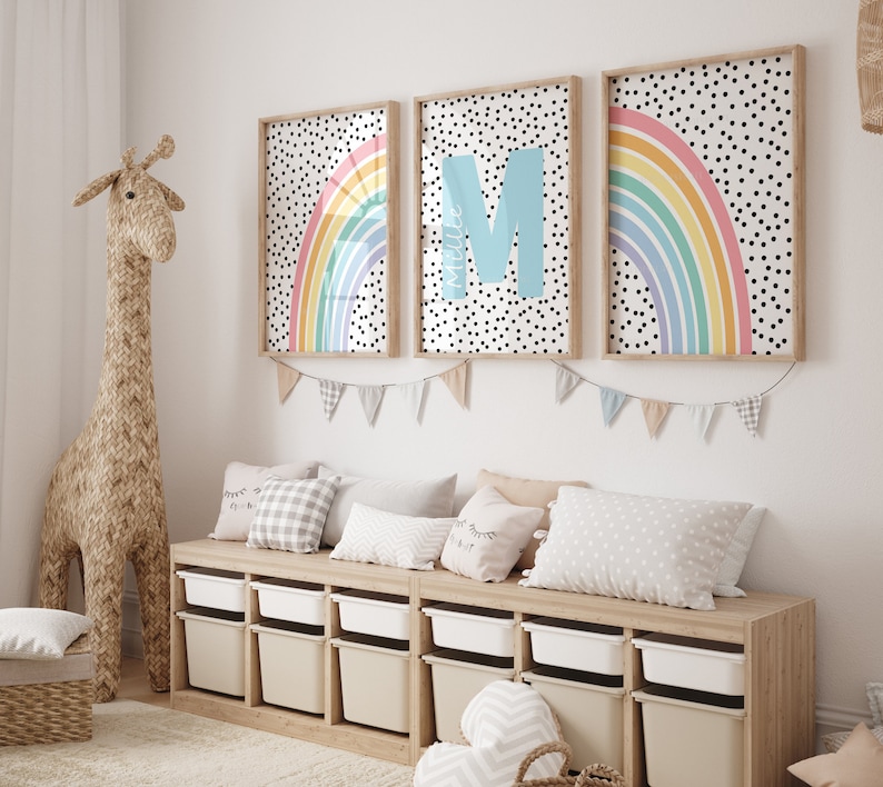 May include: A light wood storage bench with white bins and a white, grey, and black patterned cushion. Three framed prints with rainbow designs and black polka dots hang above the bench. The prints feature the letters "M" and "A".