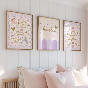 May include: Three framed wall art pieces with gold frames. The art features unicorns, hearts, stars, and text that reads "follow your dreams", "believe in yourself", "you've got this", "Amelia", and "you can do anything". The color palette includes lavender, gold, and cream.