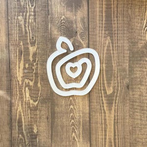 Puede incluir: Corte de madera blanco de una manzana con un corazón en su interior. La manzana está sobre un fondo de madera marrón.