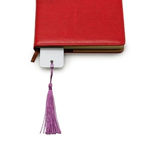 Pode incluir: Um di&aacute;rio vermelho com capa de couro com um marcador branco e uma borla roxa. O marcador est&aacute; inserido no di&aacute;rio e a borla est&aacute; pendurada. O di&aacute;rio est&aacute; fechado e as bordas das p&aacute;ginas s&atilde;o vis&iacute;veis.