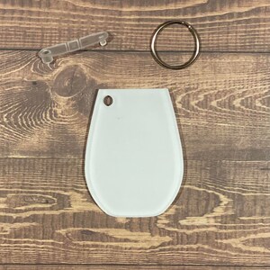 May include: White blank oval-shaped keychain with a metal ring and a clear plastic key ring attachment.