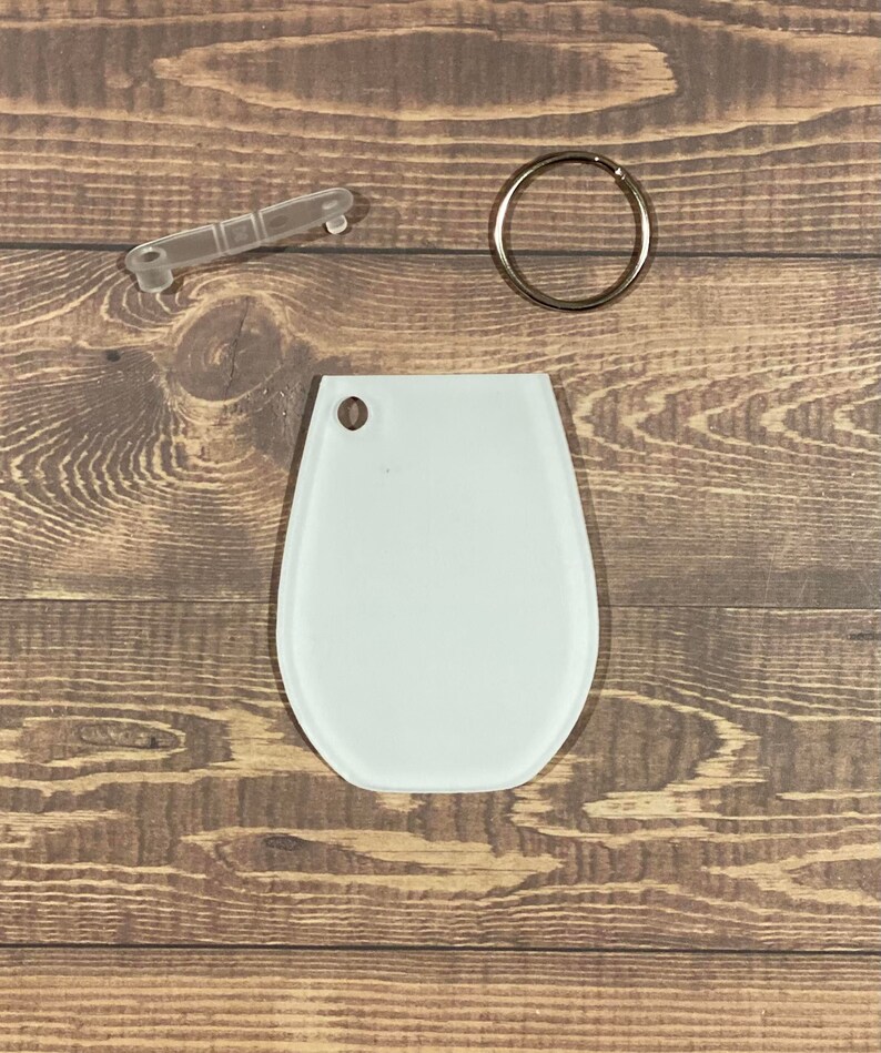 May include: White blank oval-shaped keychain with a metal ring and a clear plastic key ring attachment.