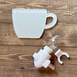 May include: White ceramic cup shaped night light with a white plug-in adapter and a clear light bulb.