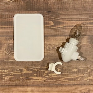 Puede incluir: Una luz nocturna de plástico blanco con una bombilla transparente. La luz nocturna está sobre una superficie de madera.