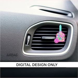 May include: A pink and blue car air freshener shaped like a paddle ball with a white polka dot ball. The air freshener is hanging from a car's air vent.