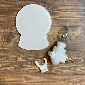 May include: White plastic nightlight shaped like a snow globe with a white plastic plug-in base and a clear light bulb.
