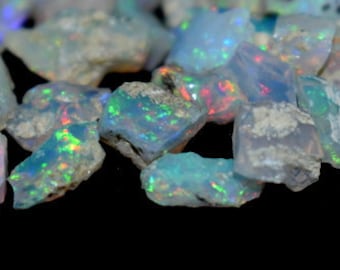 May include: A collection of iridescent opal rough, with a variety of shapes and sizes. The opals are a mix of white, blue, green, and red.