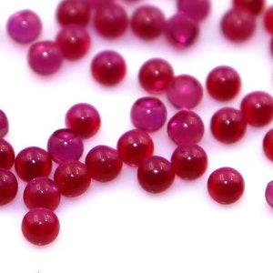 Könnte beinhalten: Eine Streuung kleiner, runder, rubinroter Perlen auf weißem Hintergrund.
