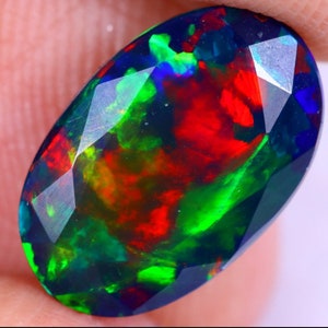 Könnte beinhalten: Ein schwarzer Opal-Edelstein mit einem facettierten Ovalschliff. Der Opal zeigt ein lebendiges Farbenspiel, darunter Rot, Grün und Blau.