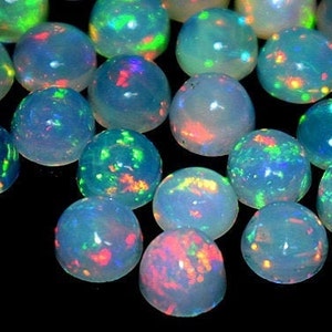 Könnte beinhalten: Eine Sammlung runder, irisierender Opal-Cabochons mit einer weißen Basis und Schimmern in Grün, Blau, Rot und Orange.
