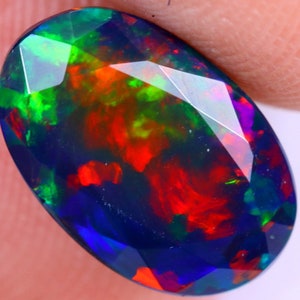 Könnte beinhalten: Ein ovaler, dunkelblauer Opal-Edelstein mit roten, grünen und blauen Schimmern.