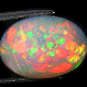 Könnte beinhalten: Ein weißer Opal-Edelstein mit einem leuchtenden Rot-, Orange- und Grüntönen. Der Opal ist oval geformt und hat eine glatte, polierte Oberfläche.