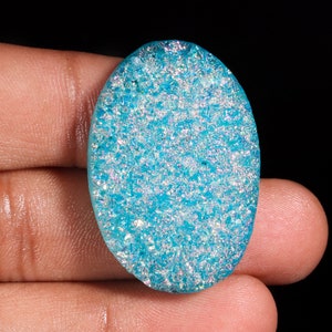 May include: A light blue oval cabochon gemstone with a sparkly, iridescent finish. The stone has a textured surface with a glittery appearance.