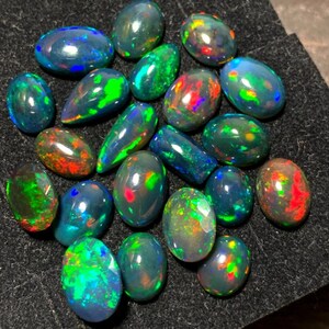 May include: A collection of black opal gemstones in various shapes and sizes. The opals display a rainbow of colors, including green, red, blue, and purple.