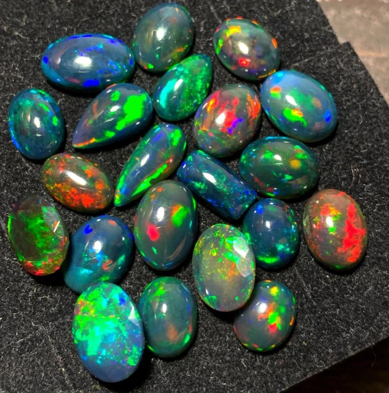 May include: A collection of black opal gemstones in various shapes and sizes. The opals display a rainbow of colors, including green, red, blue, and purple.