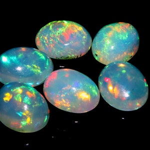 May include: Six oval-shaped opals with a rainbow iridescent sheen. The opals are a light blue color with flashes of green, red, and yellow.