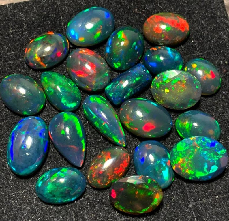 May include: A collection of black opal gemstones in various shapes and sizes. The opals have a dark base with flashes of green, blue, red, and orange.