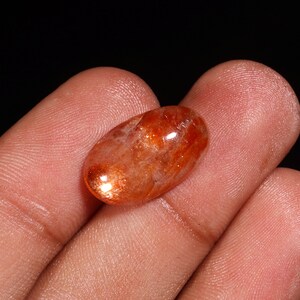 Puede incluir: Un cabujón de piedra de sol de gran tamaño, de forma ovalada, de color rojo-naranja y con un brillo brillante e iridiscente.