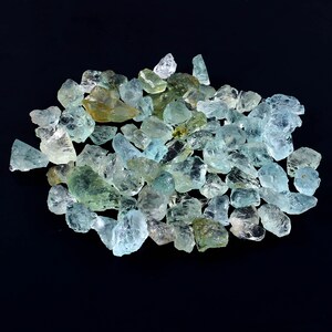 May include: A large pile of aquamarine gemstones, with a variety of shapes and sizes. The stones are a light blue-green color and have a translucent appearance.
