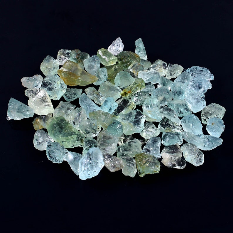 May include: A large pile of aquamarine gemstones, with a variety of shapes and sizes. The stones are a light blue-green color and have a translucent appearance.